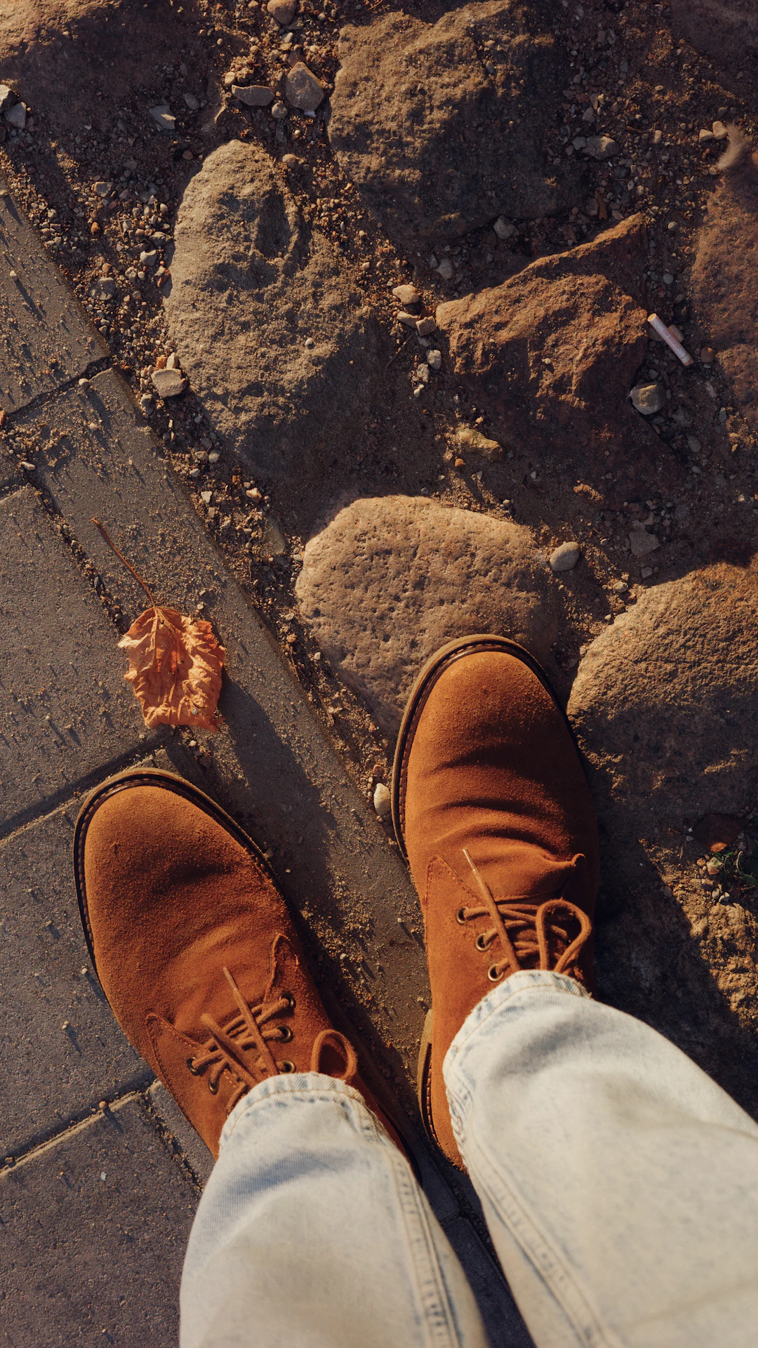 Brown suede boots and light jeans on cobblestone path.
